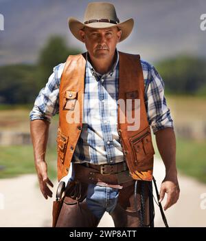 Portrait, serious cowboy and man at farm in the rural countryside to draw gun in Texas. Ranch, confidence and male person in western hat outdoor in Stock Photo