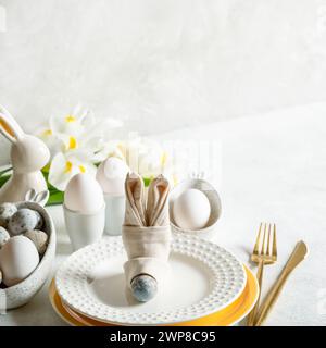 Easter card template with elegant table setting. Napkin as bunny muzzle, figured plates, natural colors eggs, white Iris flowers, bunny, golden cutler Stock Photo