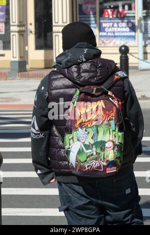 Man crossing Main St in Ossining, New York wearing a backpack that says Wubba Lubba Dub Dub which means 'I'm in Pain. Help me.' From Risky Business. Stock Photo