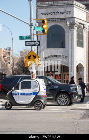 HUGE TINY. a large Cadillac Denali parked behind a tiny 3 wheel Chaverim mini-vehicle outside a Satmar synagogue i Williamsburg, Brooklyn, New York. Stock Photo