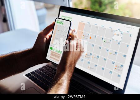 Man looking at calendar on phone and laptop, early in the morning for planning the day. Digital schedule concept. Stock Photo