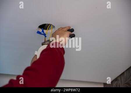 young man repairing ceiling spotlight holding the peeler to cut wires and reattach them with new ones Stock Photo