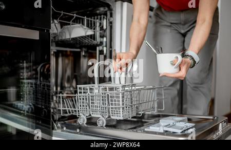 Young Woman Is Loading Spoons Into Dishwasher In Close-Up View Stock Photo