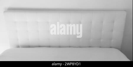 Soft headboard. Upholstery for furniture made of genuine or artificial leather and quilted fabric. Soft headboard against a light wall. Black and whit Stock Photo