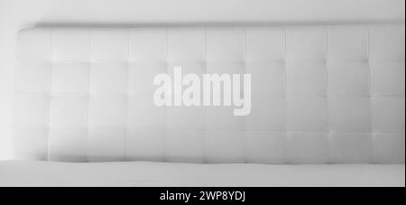 Soft headboard. Upholstery for furniture made of genuine or artificial leather and quilted fabric. Soft headboard against a light wall. Black and whit Stock Photo