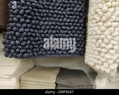 White and gray microfiber bath mats hang on a store counter. Scandinavian interior style. Soft pimply textile rectangular rugs with knitted pimples. D Stock Photo