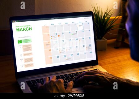 Monthly planner schedule. Man looking at digital calendar on laptop screen, at night to plan the next day. Stock Photo