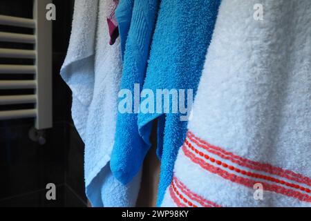 Towels hang next to a heated towel rail, wall radiator or radiator. White, blue, pink, red towels. Organization of household items in the bathroom Stock Photo