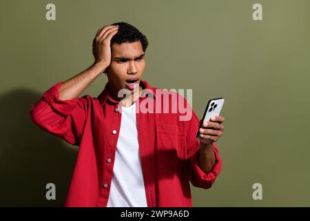 Photo of funky impressed man dressed red shirt getting dislikes modern device empty space isolated green color background Stock Photo