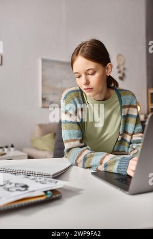 Teen girl engaged in e-learning with her notebook and laptop at a cozy home setting, digital age Stock Photo
