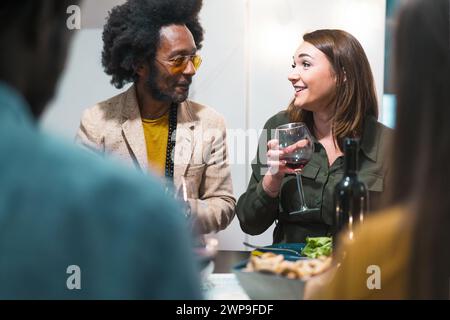 Multicultural friends in casual wear enjoying wine and conversation at an indoor party - Sharing stories and laughter over glasses of red wine. Stock Photo