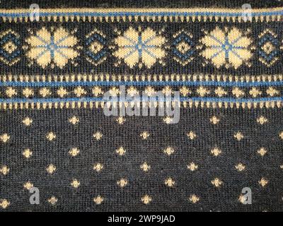 A fragment of an ornament on a knitted polyester or woolen sweater. Flowers. Winter motives. Blue threads for hand knitting. White thread knitted Stock Photo