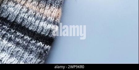 Knitted warm product such as a scarf or hat on a gray background. Knitting with multi-colored yarn. White, gray, brown, beige and black stripes and Stock Photo