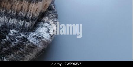 Knitted warm product such as a scarf or hat on a gray background. Knitting with multi-colored yarn. White, gray, brown, beige and black stripes and Stock Photo