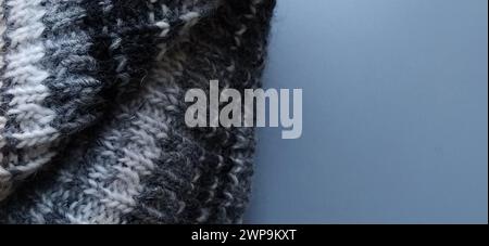 Knitted warm product such as a scarf or hat on a gray background. Knitting with multi-colored yarn. White, gray, brown, beige and black stripes and Stock Photo