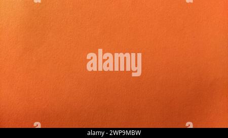 A sheet of thick paper of bright orange color. Close-up. Background intense shade. Natural lateral lighting. Fine cardboard or paper texture. Light Stock Photo