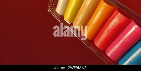 Multi-colored new plasticine in plastic packaging on a red background. Plasticine plates of red, pink, green, white, yellow, brown, blue, black. Set Stock Photo