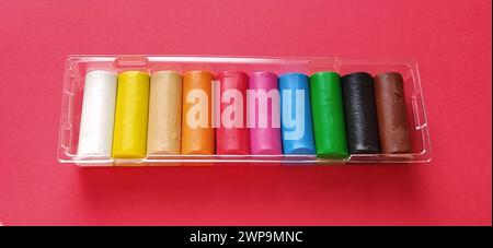 Multi-colored new plasticine in plastic packaging on a red background. Plasticine plates of red, pink, green, white, yellow, brown, blue, black. Set Stock Photo