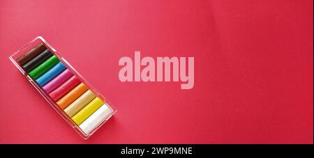 Multi-colored new plasticine in plastic packaging on a red background. Plasticine plates of red, pink, green, white, yellow, brown, blue, black. Set Stock Photo
