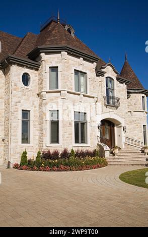 Partial view of luxurious two story beige and tan cut stone home with landscaped front yard and paving stone driveway in summer. Stock Photo