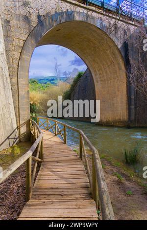 wooden footbridge over a mountain river with a stone tunnel in the background Stock Photo
