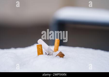 A close-up view of a pile of discarded cigarette butts on snow. Stock Photo