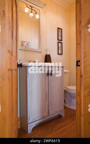 Bleached wooden antique style vanity in bathroom with brown stained wood plank floorboard inside reproduced old home. Stock Photo