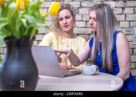 Two professional women engage in a serious business planning session over a laptop, with a vase of bright tulips suggesting growth and a fresh approac Stock Photo