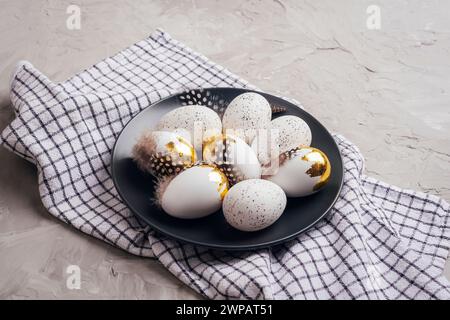 Easter eggs on black plate, checkered napkin on concrete gray table. Top view. Stock Photo