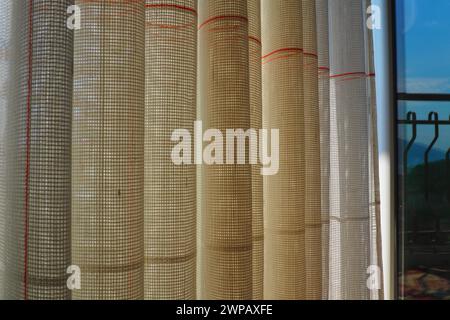 White coarse cotton or linen curtains made of weaves of thin threads. Simple compact economical apartment interior. Window decoration in the room. Red Stock Photo