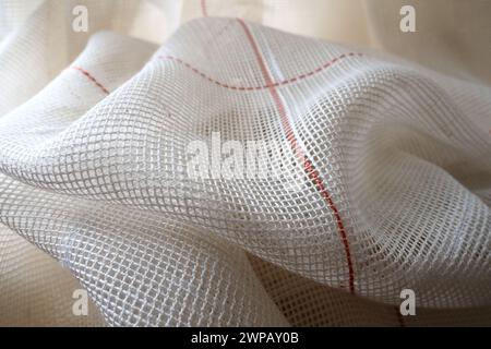 White coarse cotton or linen curtains made of weaves of thin threads. Simple compact economical apartment interior. Window decoration in the room. Red Stock Photo