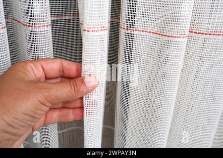 White coarse cotton or linen curtains made of weaves of thin threads. Simple compact economical apartment interior. Window decoration in the room. A Stock Photo