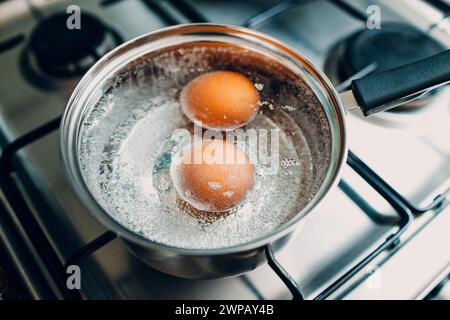 Saucepan stainless steel with two boiling eggs breakfast in a water on a gas stove top view. Stock Photo