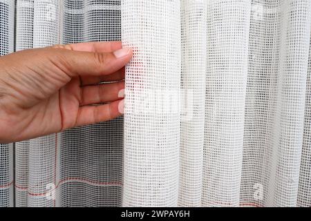 White coarse cotton or linen curtains made of weaves of thin threads. Simple compact economical apartment interior. Window decoration in the room. A Stock Photo