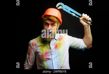 Construction worker or builder in hard hat with adjustable pipe wrench. Bearded man in protective helmet with adjustable spanner. Technician, repairer Stock Photo