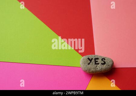 Pebble stone with text yes on them. Colorful background from sheets of paper. Stock Photo