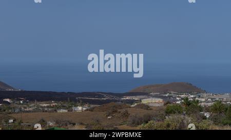 A scenic view of a coastal town and the ocean, with a cold lava flow on the mountainside. Stock Photo