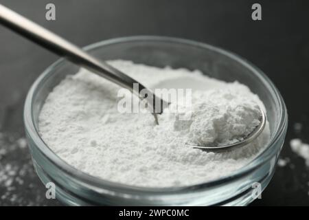 Baking powder in bowl and spoon on black table, closeup Stock Photo