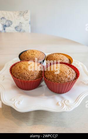 Four homemade fresh-baked banana nut muffins in silicone cups on a white plate. USA. Stock Photo