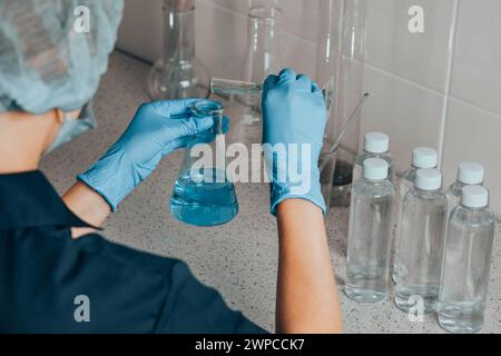 woman in protective cap in laboratory checks water quality using glass tube filled with blue chemical liquid for research and analysis in lab Stock Photo