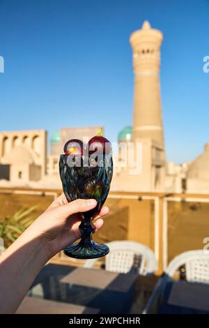 Woman holding  in hand glass full of figs at roof top restaurant in Bukhara against Kalyan Minaret in Uzbekistan Stock Photo