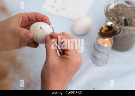 Female hands paint a white Easter egg according to Sorbian tradition with a trimmed goose quill and melted bee and candle wax, copy space Stock Photo
