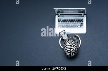 Steel brain with small hands, skillfully holding a mobile phone while working at a laptop isolated on black background with copy space. Artificial int Stock Photo
