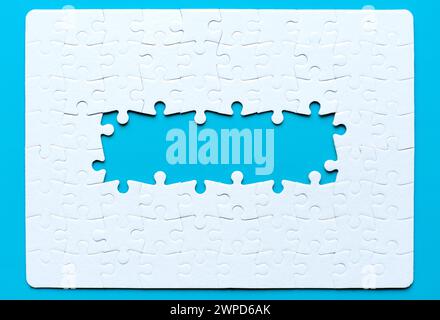 Assembled blank jigsaw puzzle with several missing pieces at the center arranged on a pristine blue background. Unity and progression related concept. Stock Photo
