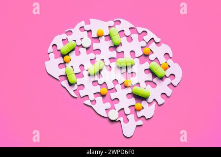 Colorful pills scattered on a disassembled brain puzzle isolated on pink backdrop. Mental health and medication concept. Stock Photo