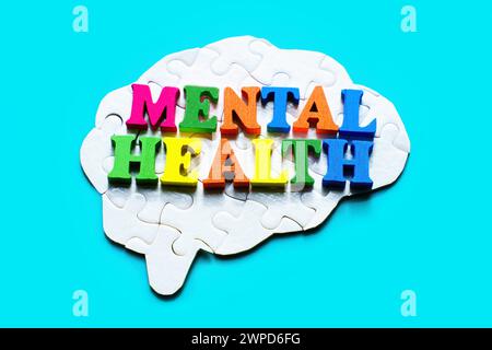 Assembled brain-shaped jigsaw puzzle on a light blue background with the words 'Mental Health' spelled out in colorful wooden letters. Mental well-bei Stock Photo