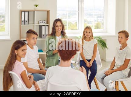 Friendly counselor is talking to group of junior high school students at psychological session. Stock Photo