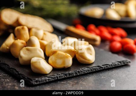 Smoked mini scamorza cheese. Traditional italian cheese on cutting board on the black table. Stock Photo