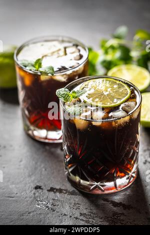 Tropical alcoholic cocktail Cuba Libre composed of white rum, cola, ice cubes, lime and mint. Stock Photo