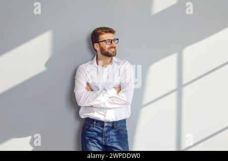 Portrait of bearded man in eyeglasses standing at wall with crossed arms Stock Photo